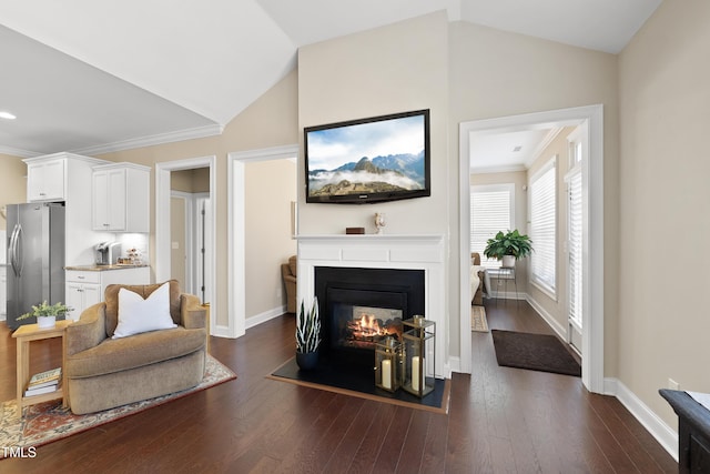 living area featuring baseboards, a fireplace with flush hearth, dark wood-style flooring, vaulted ceiling, and crown molding