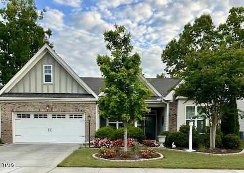 craftsman inspired home with board and batten siding, driveway, brick siding, a garage, and a front lawn