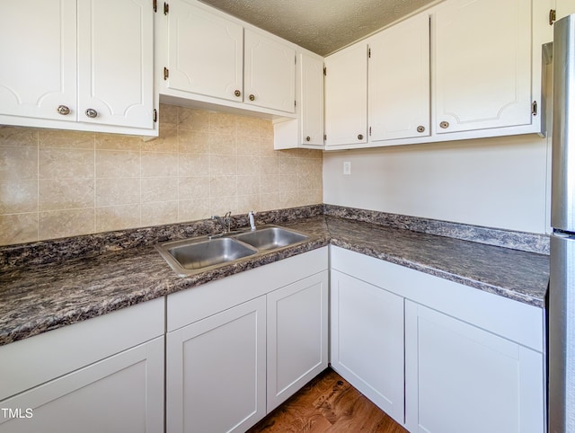 kitchen with tasteful backsplash, dark countertops, dark wood-type flooring, white cabinetry, and a sink