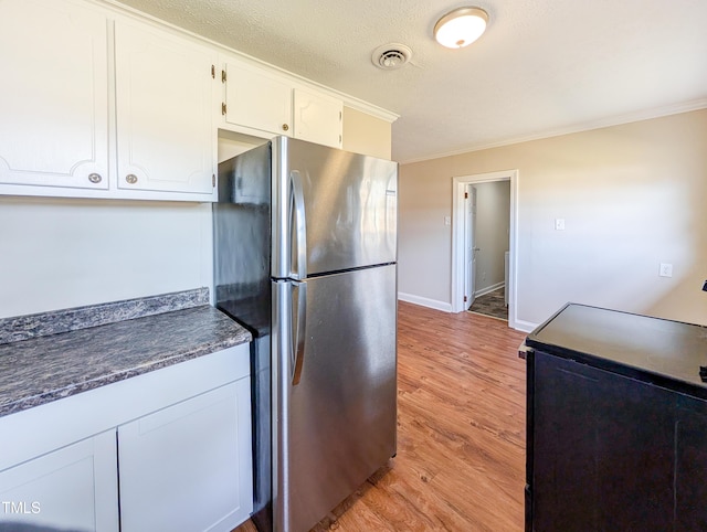 kitchen with white cabinetry, light wood-style floors, freestanding refrigerator, dark countertops, and crown molding