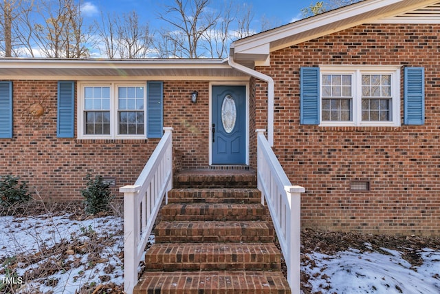 snow covered property entrance featuring brick siding and crawl space