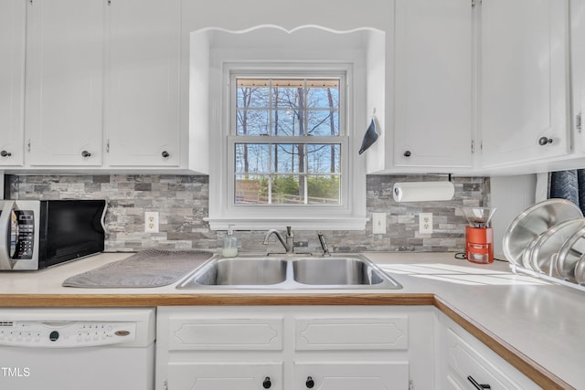 kitchen with light countertops, stainless steel microwave, white cabinets, white dishwasher, and a sink