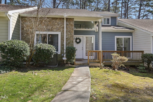 property entrance with stone siding, a shingled roof, and a lawn