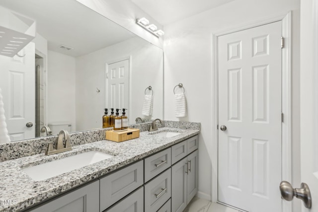 bathroom with marble finish floor, double vanity, a sink, and baseboards