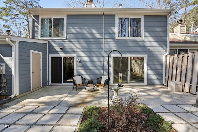 back of property featuring a fire pit, a patio area, fence, and a chimney