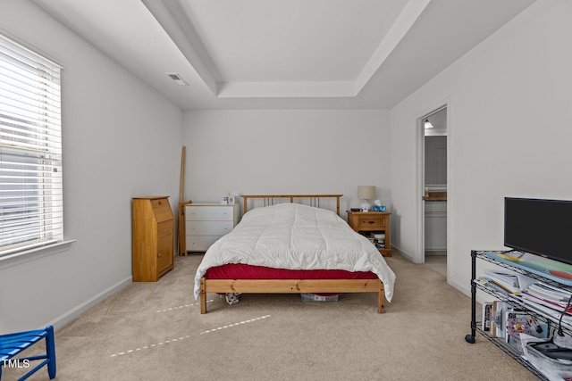 carpeted bedroom featuring baseboards, visible vents, a raised ceiling, and ensuite bathroom