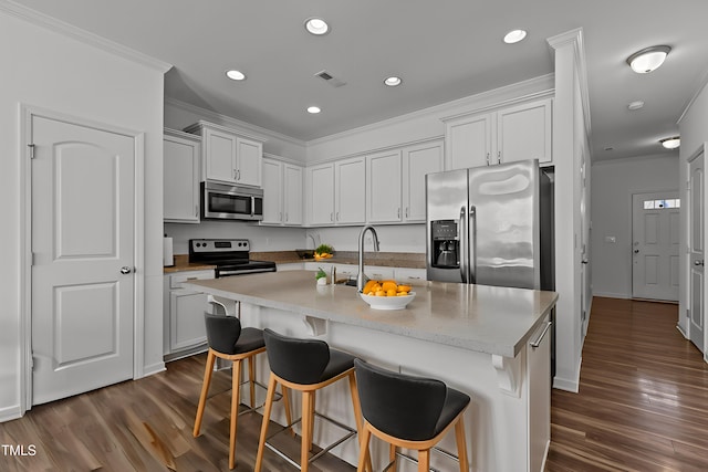 kitchen featuring visible vents, appliances with stainless steel finishes, a kitchen breakfast bar, dark wood-style flooring, and ornamental molding