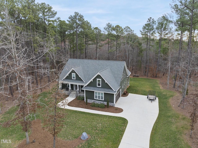 view of front of home featuring a front lawn, a porch, a wooded view, concrete driveway, and a shingled roof