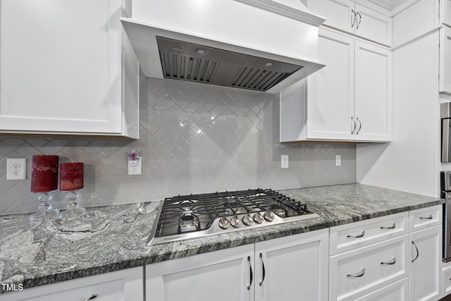 kitchen with white cabinetry, extractor fan, stainless steel gas stovetop, and dark stone countertops