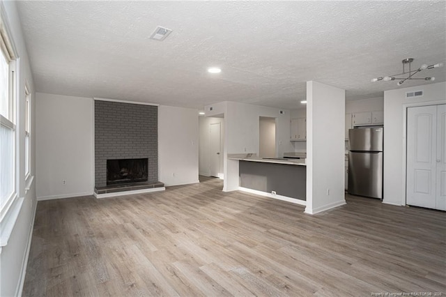 unfurnished living room with light wood finished floors, visible vents, a brick fireplace, a textured ceiling, and baseboards