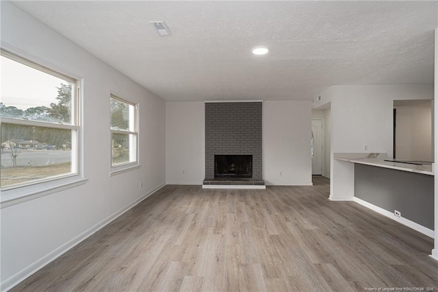 unfurnished living room featuring visible vents, a brick fireplace, a textured ceiling, light wood-type flooring, and baseboards