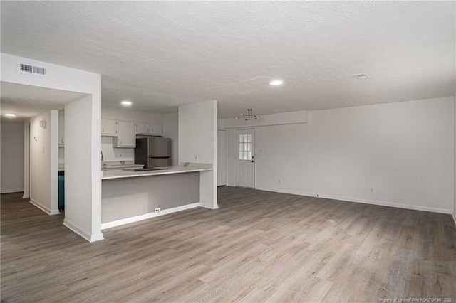 kitchen with light countertops, visible vents, freestanding refrigerator, open floor plan, and a peninsula