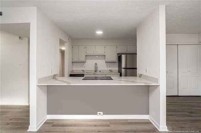 kitchen with light stone counters, wood finished floors, freestanding refrigerator, a peninsula, and black electric cooktop