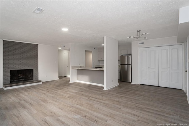 unfurnished living room featuring light wood-type flooring, a fireplace, visible vents, and a textured ceiling