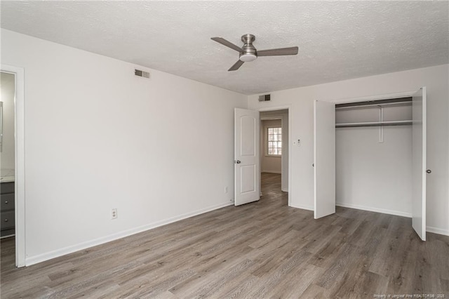 unfurnished bedroom with a closet, visible vents, a textured ceiling, and wood finished floors