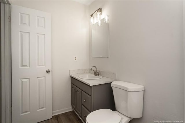 bathroom featuring toilet, baseboards, wood finished floors, and vanity