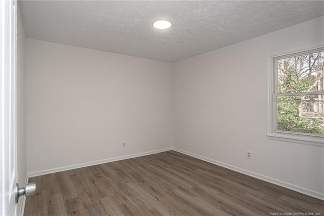 spare room featuring dark wood-style flooring, a textured ceiling, and baseboards