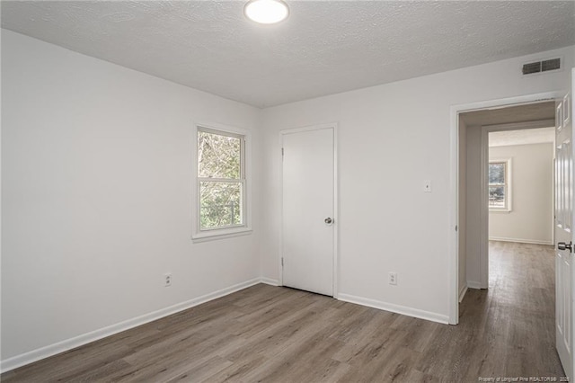 unfurnished room featuring visible vents, a textured ceiling, baseboards, and wood finished floors