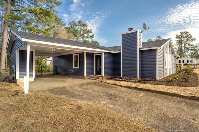 rear view of house with dirt driveway, a carport, a chimney, and entry steps