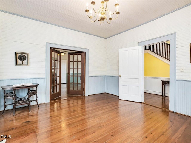 spare room featuring an inviting chandelier, french doors, hardwood / wood-style floors, and wainscoting