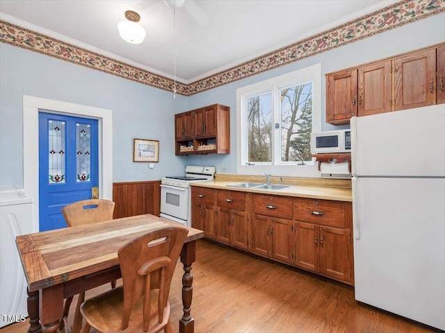 kitchen featuring white appliances, a sink, light countertops, light wood finished floors, and brown cabinetry