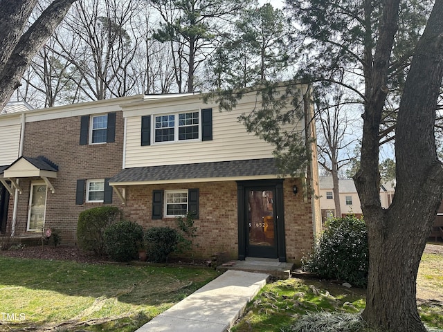 view of front of home with a front yard, brick siding, and roof with shingles