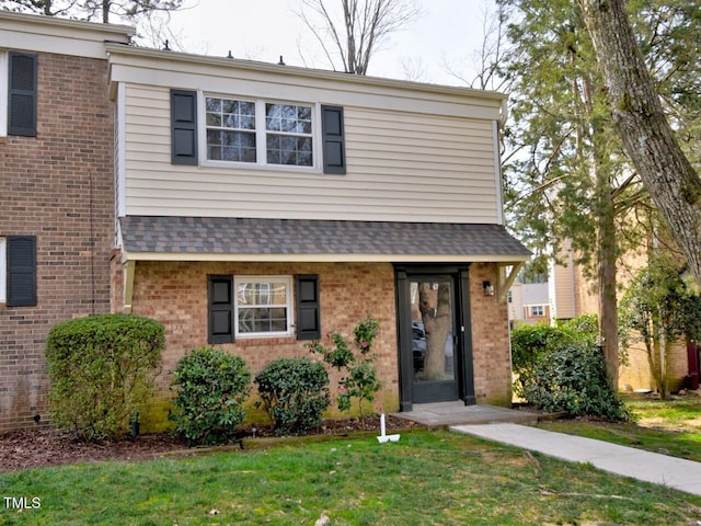 view of front of home featuring brick siding, a front yard, and roof with shingles