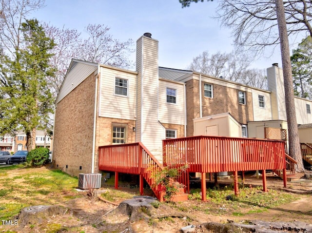 rear view of house with a deck, cooling unit, brick siding, and a chimney