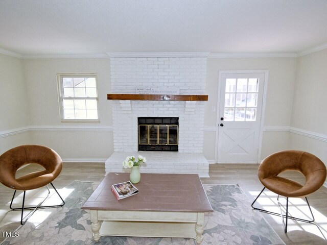 living room with a brick fireplace, wood finished floors, baseboards, and ornamental molding