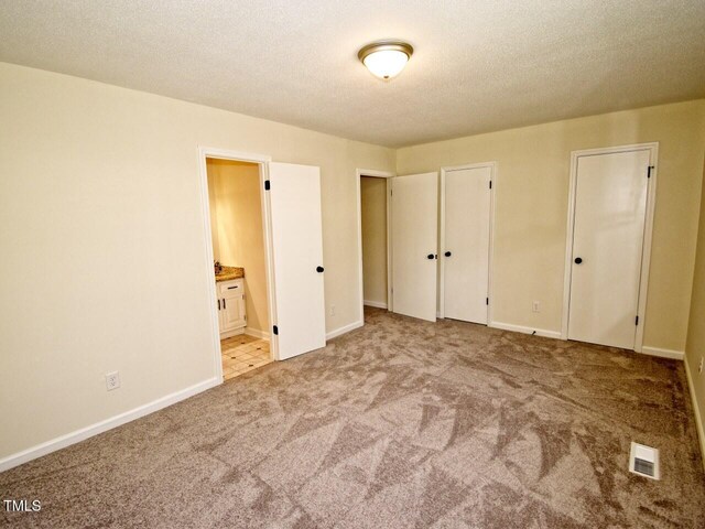 unfurnished bedroom featuring visible vents, connected bathroom, baseboards, carpet, and a textured ceiling