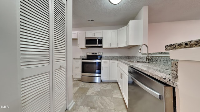 kitchen featuring a sink, visible vents, white cabinetry, appliances with stainless steel finishes, and light stone countertops