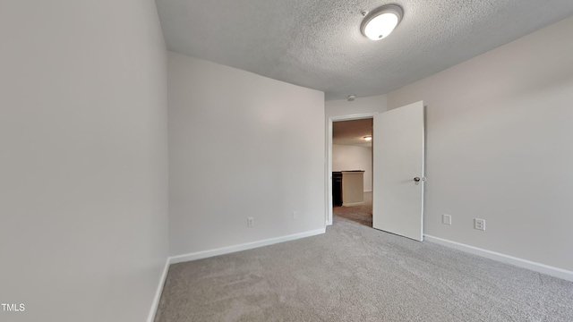 spare room with light carpet, a textured ceiling, and baseboards