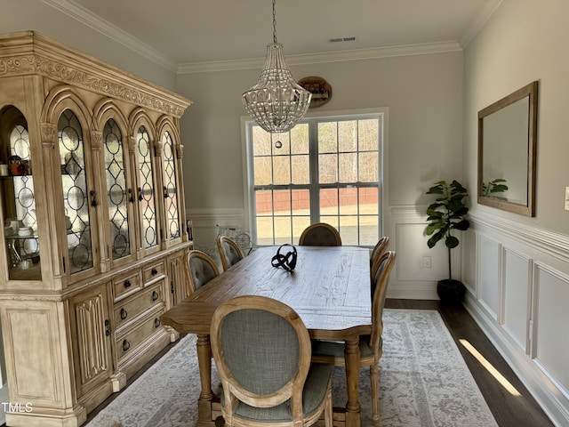 dining area featuring a wainscoted wall, visible vents, dark wood-style flooring, and ornamental molding