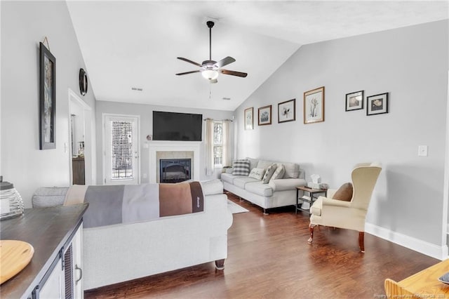 living room featuring a fireplace, baseboards, ceiling fan, dark wood-style flooring, and vaulted ceiling