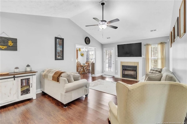 living room with dark wood finished floors, visible vents, a tile fireplace, and vaulted ceiling