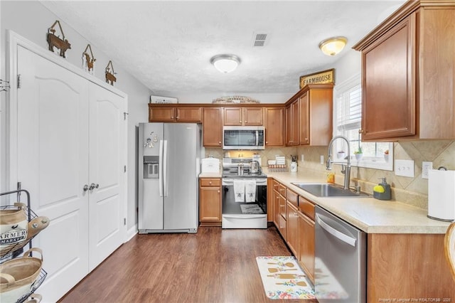 kitchen featuring dark wood-style flooring, a sink, stainless steel appliances, light countertops, and brown cabinets