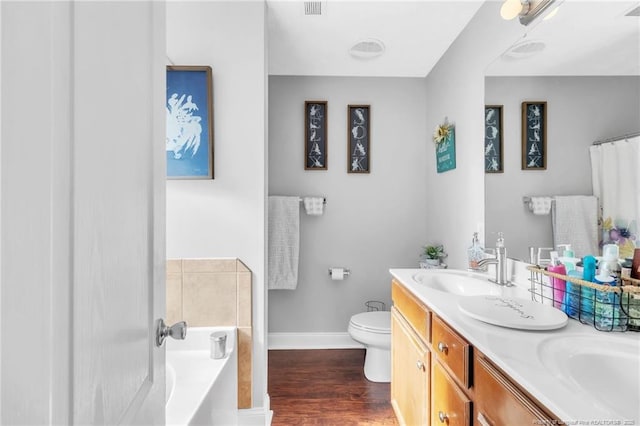 full bath with wood finished floors, baseboards, a sink, a garden tub, and toilet