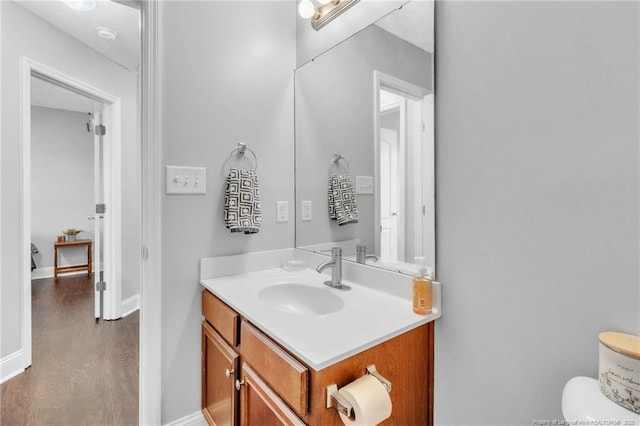 half bathroom featuring baseboards, toilet, wood finished floors, and vanity