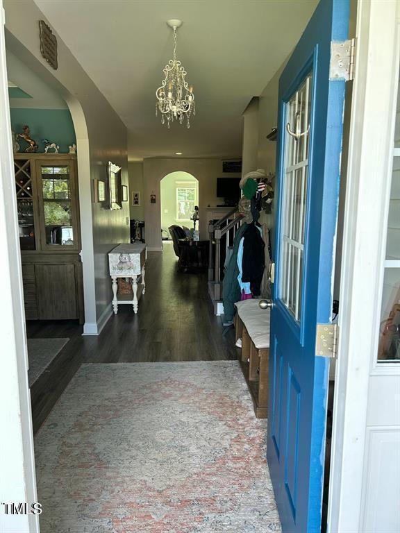 foyer entrance featuring an inviting chandelier, arched walkways, and dark wood-style flooring