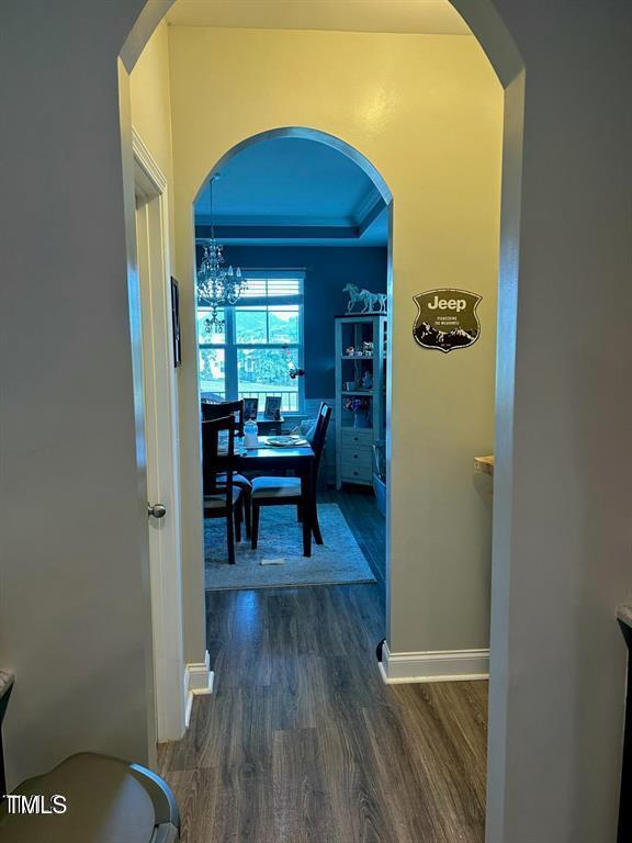 corridor featuring arched walkways, baseboards, a raised ceiling, and dark wood-style flooring