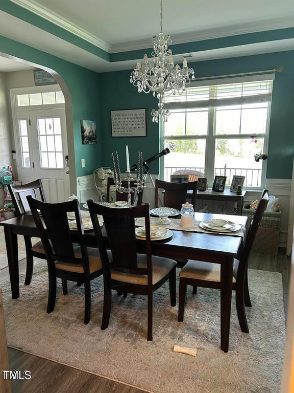 dining room featuring arched walkways, wainscoting, wood finished floors, a tray ceiling, and crown molding