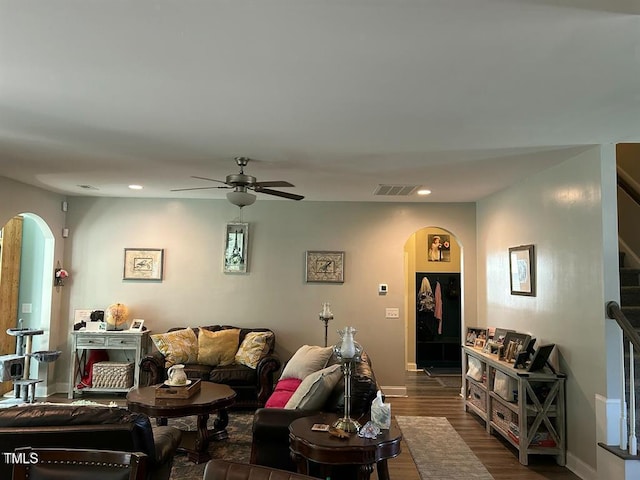 living room featuring arched walkways, dark wood-style flooring, visible vents, stairway, and a ceiling fan