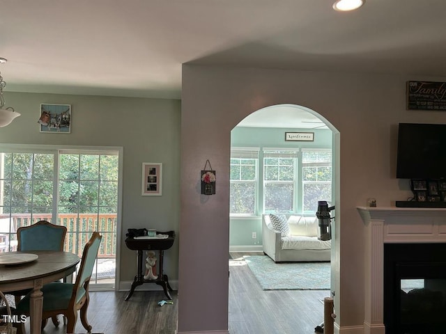 dining space with baseboards, arched walkways, wood finished floors, and a multi sided fireplace