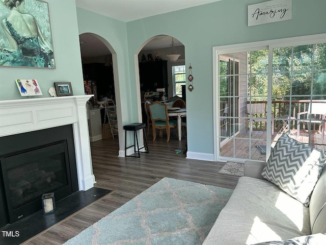 living room with a fireplace with flush hearth, arched walkways, dark wood finished floors, and baseboards