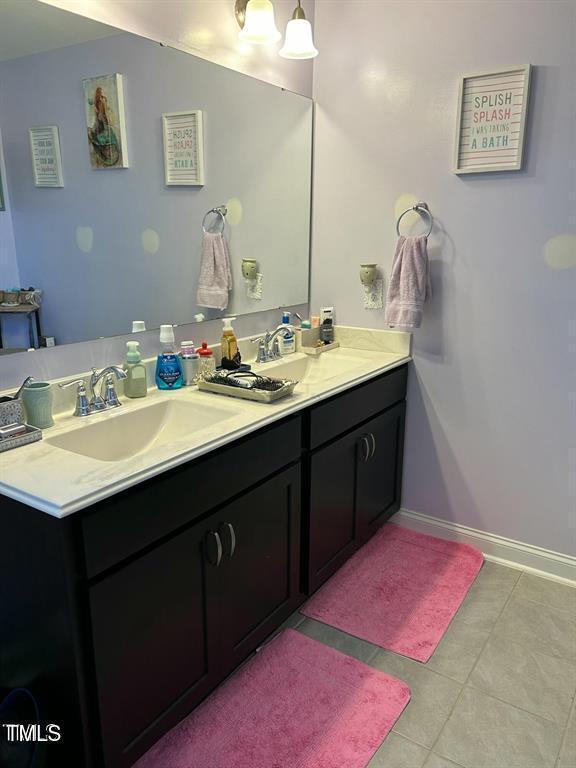 full bathroom with baseboards, double vanity, a sink, and tile patterned floors