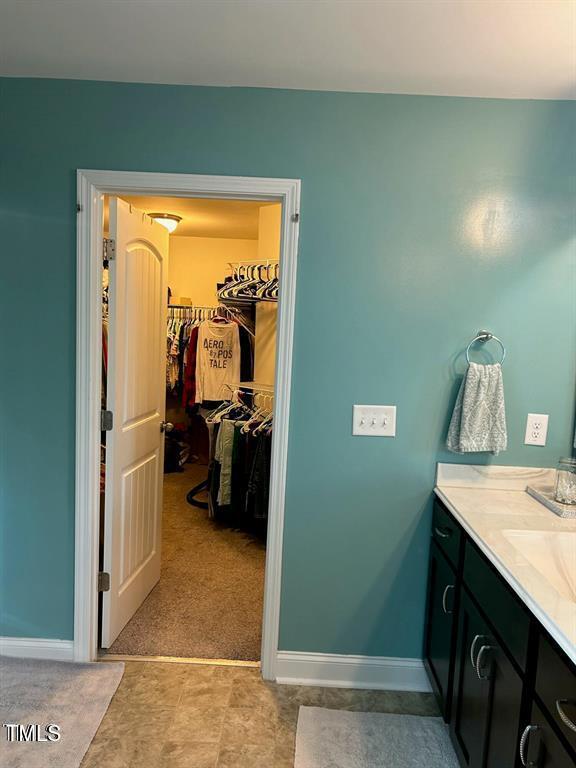 bathroom with a spacious closet, vanity, and baseboards