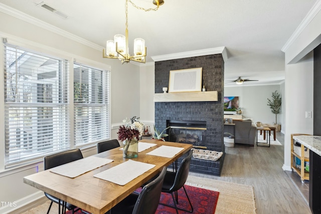 dining area with a brick fireplace, visible vents, wood finished floors, and ornamental molding