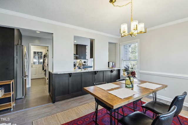 dining space with ornamental molding, light wood finished floors, baseboards, and a notable chandelier