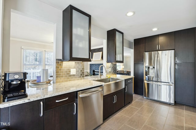 kitchen with decorative backsplash, appliances with stainless steel finishes, glass insert cabinets, a sink, and light stone countertops