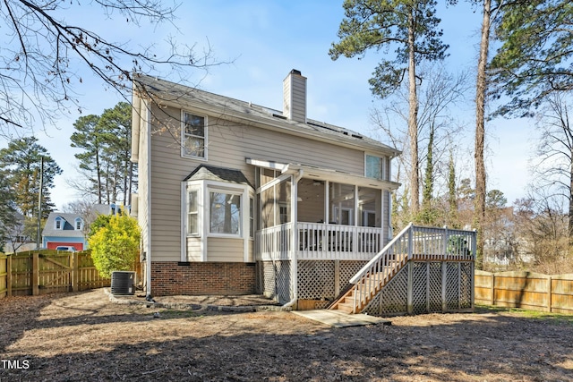 back of house with a sunroom, a fenced backyard, a chimney, stairway, and brick siding